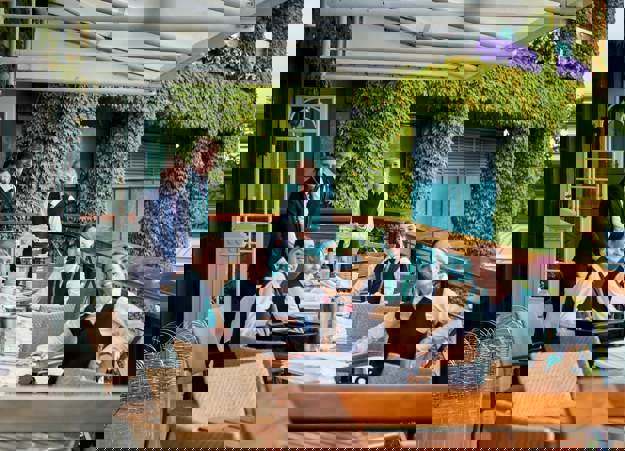 A group of Constellation's hospitality staff, sat at tables on a balcony at Wimbledon, smiling at the camera.